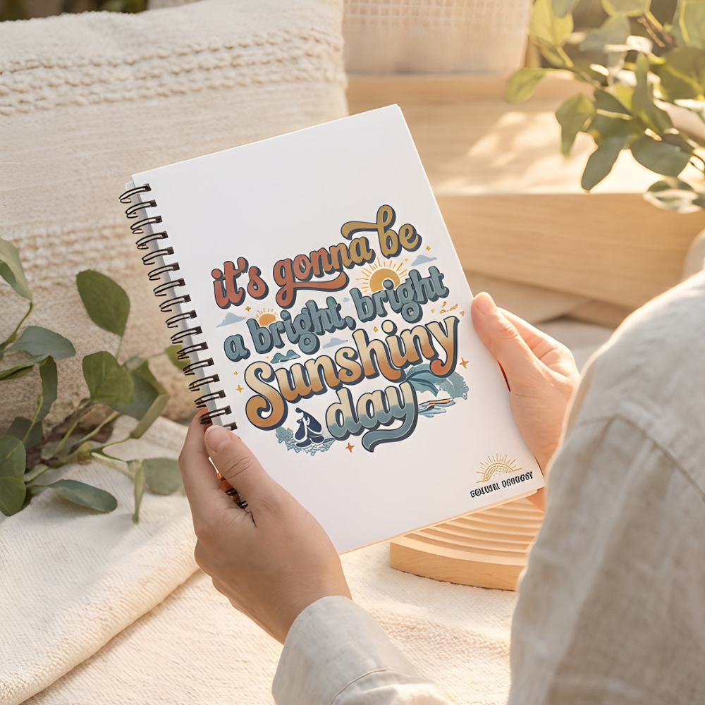Person holding a notebook with 'It's gonna be a bright, bright sunny day' text in an outdoor setting.