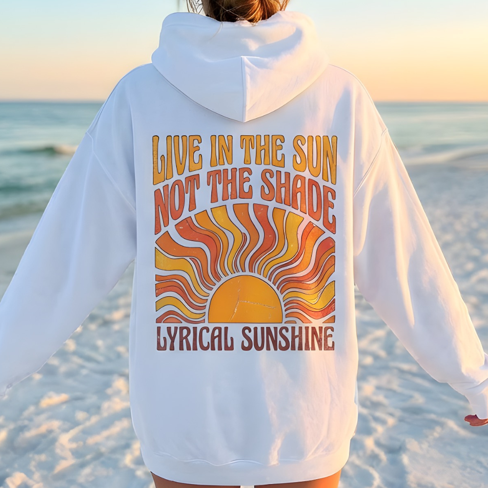 Person wearing a white hoodie with a sun graphic and text on a beach