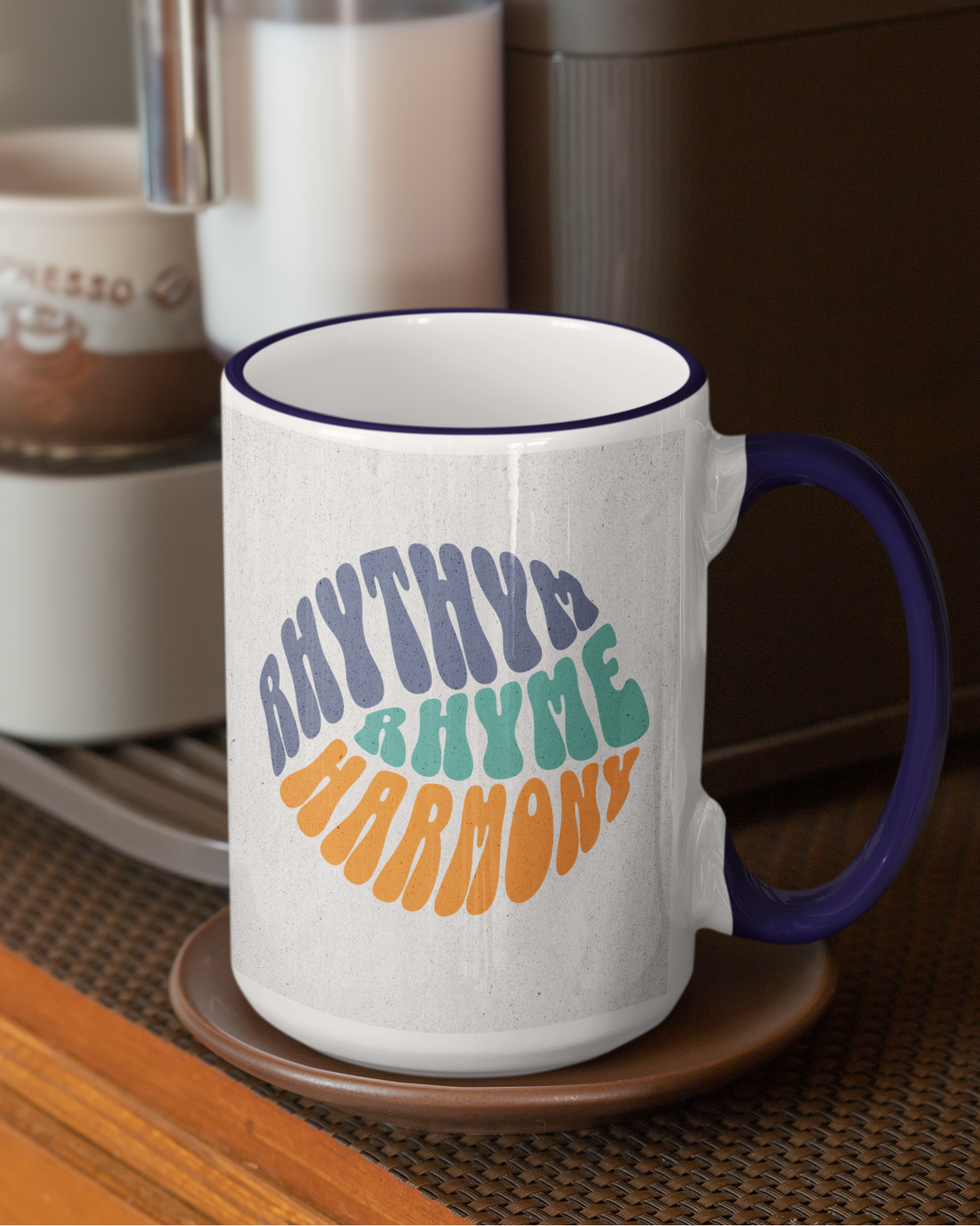 White mug with colorful text 'RHYTHM RHYME HARMONY' on a wooden surface with a coffee maker in the background.