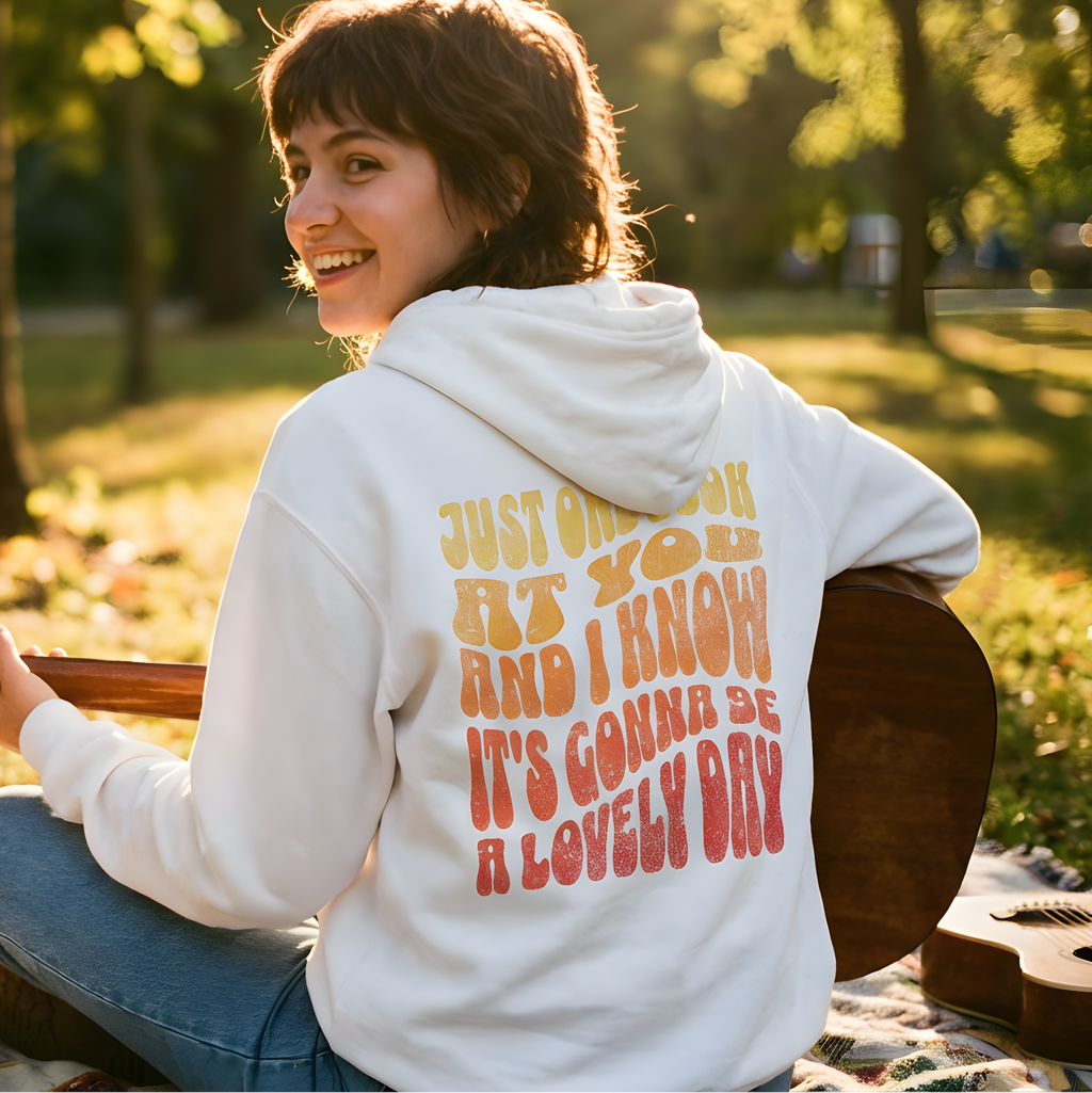 Person wearing a hoodie with text, sitting outdoors with a guitar, and promotional text for a hoodie brand.