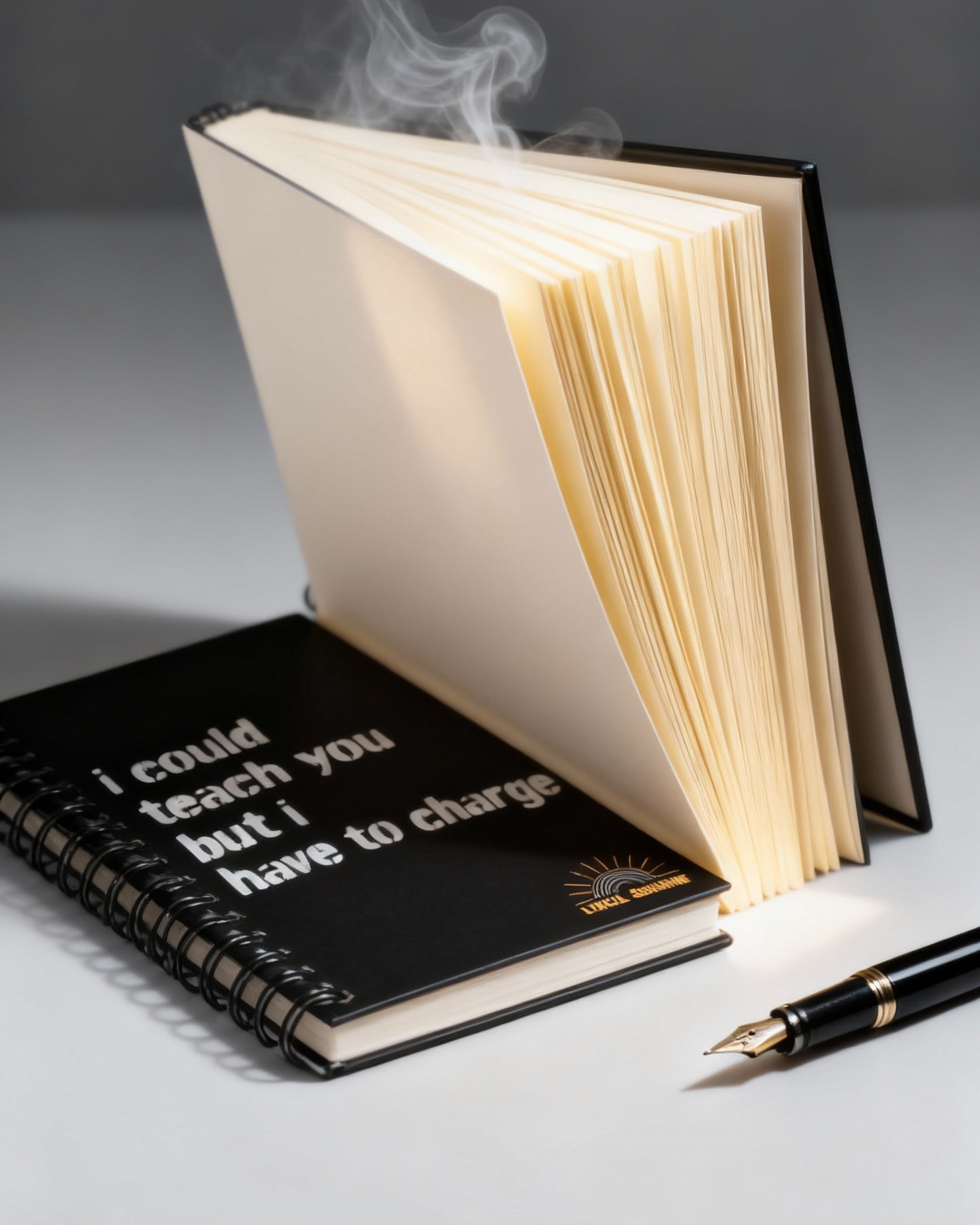 Open book with smoke coming out, next to a black notebook with text and a pen on a gray background