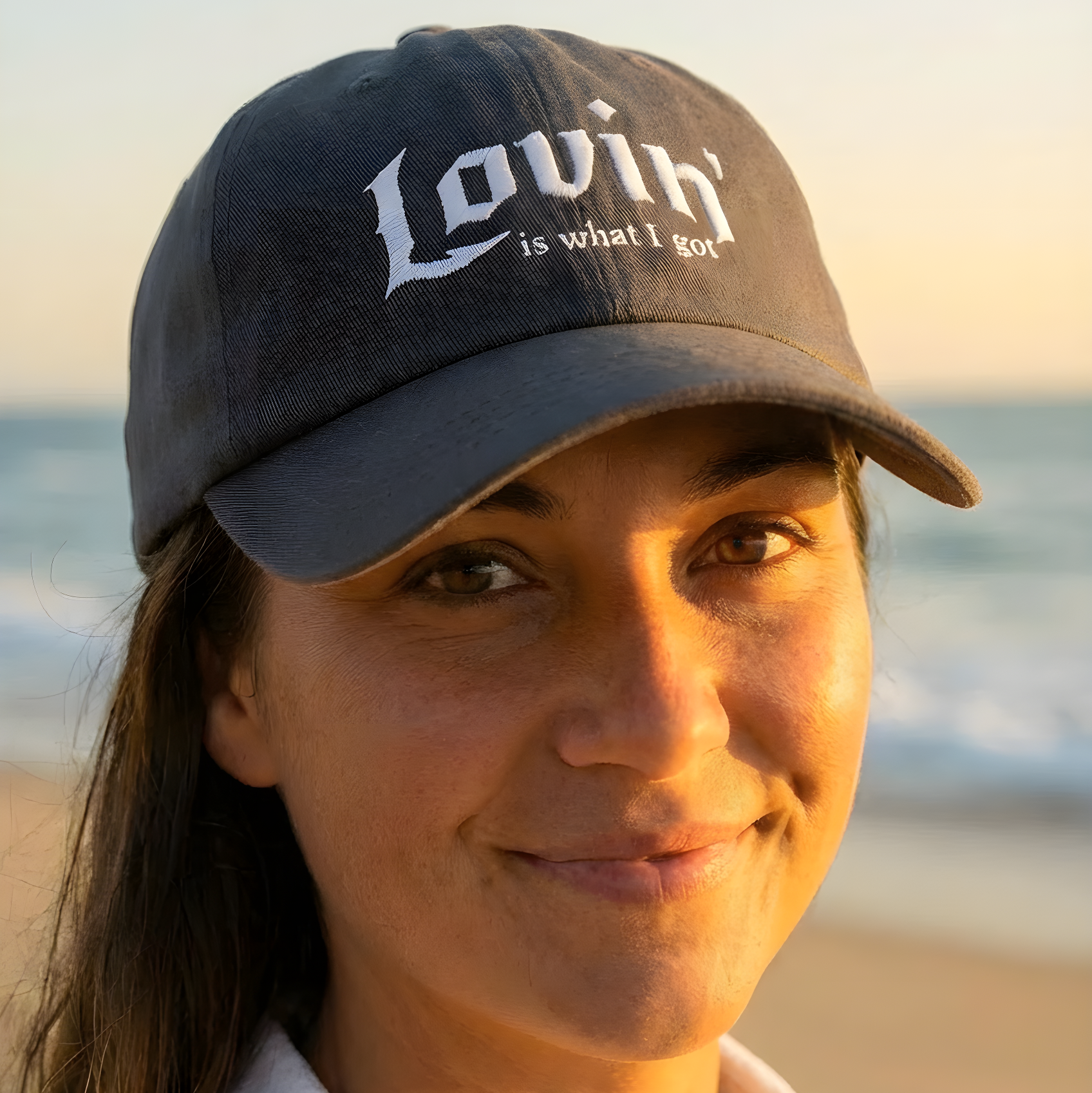 Woman wearing a cap with 'Lovin' is what I got' text on a beach