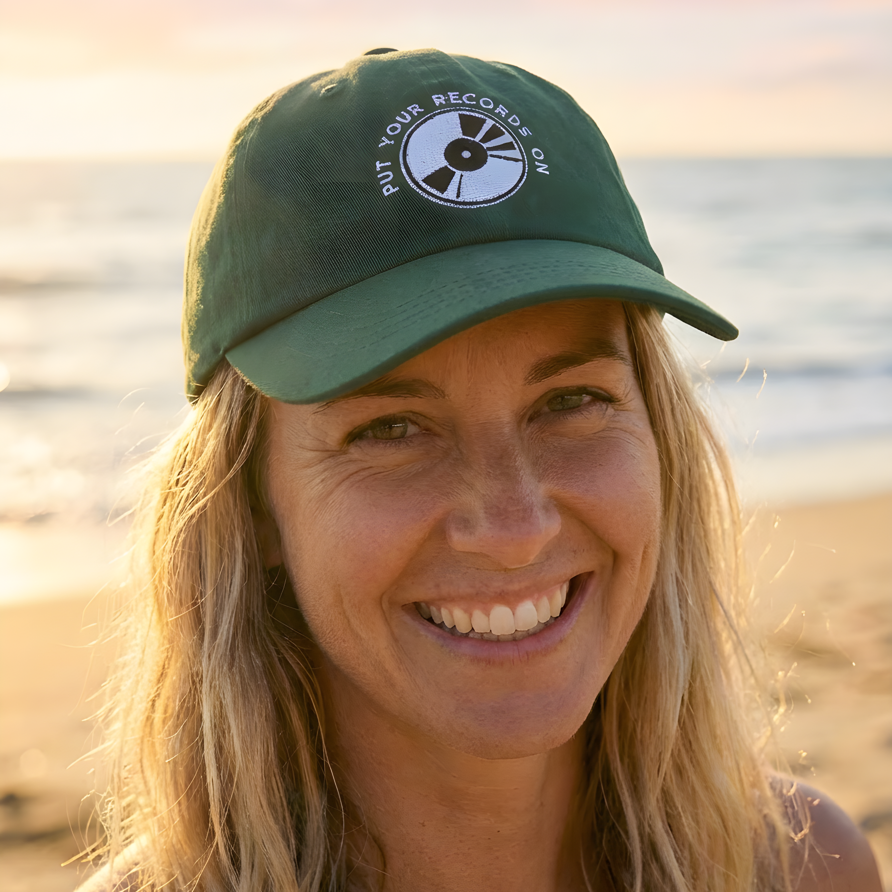 Person wearing a green cap with a logo on a beach at sunset