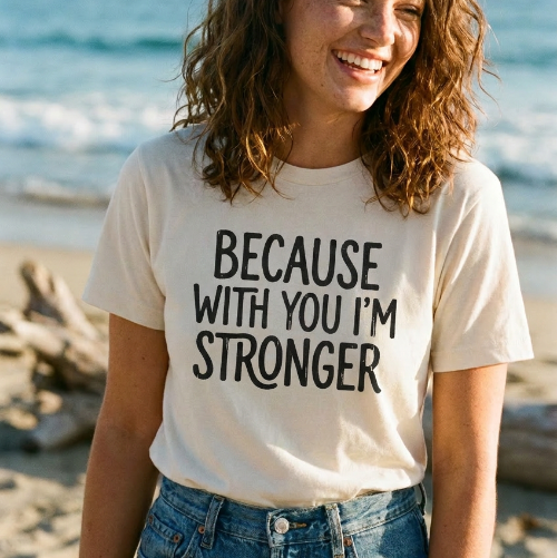 Woman wearing a t-shirt with 'Because with you I'm stronger' text on a beach, with Lyrical Sunshine logo.
