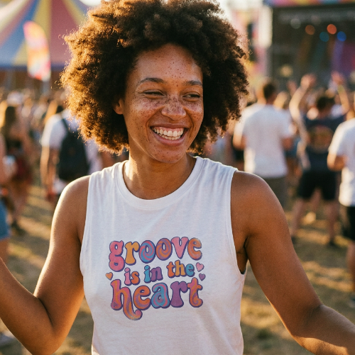 Woman wearing a 'Groove is in the Heart' tank top at a festival with colorful tents in the background.