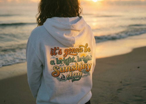 Person wearing a hoodie with text on the beach at sunset