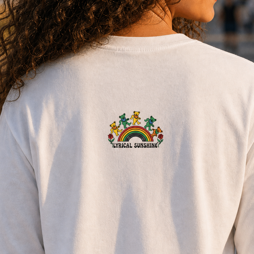 A close-up back view of a person wearing a white long-sleeve sweatshirt with a colorful 'African Sunshine' graphic on the upper back. The graphic features a rainbow, dancing figures, and sun motifs.