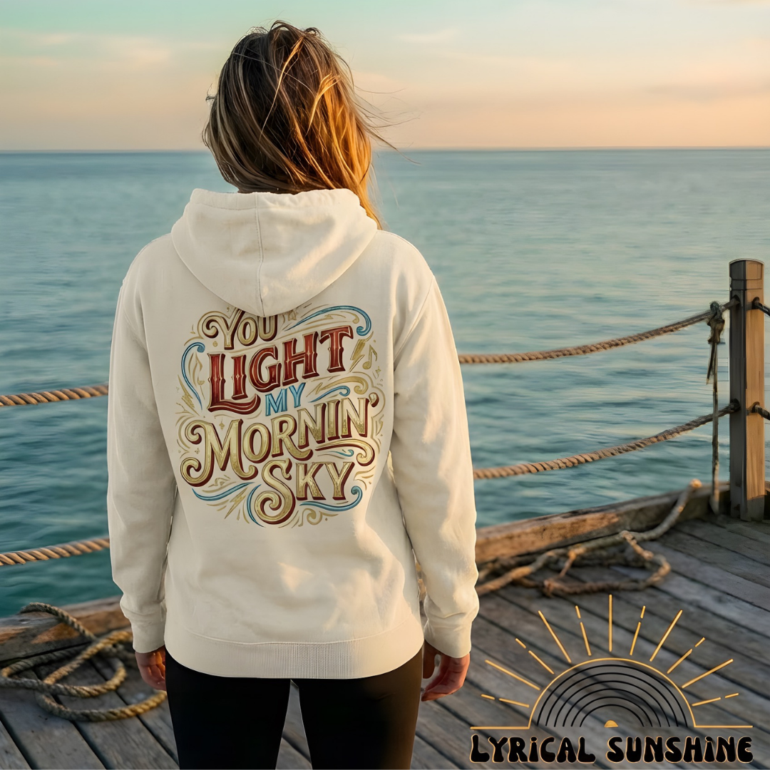 Person wearing a hoodie with text by the ocean at sunset