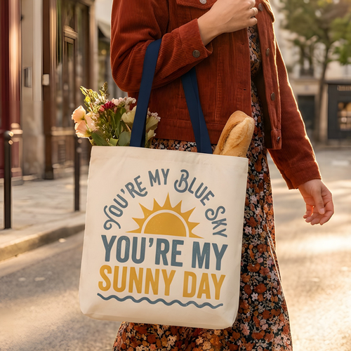 Woman holding a tote bag with a motivational quote on a city street.