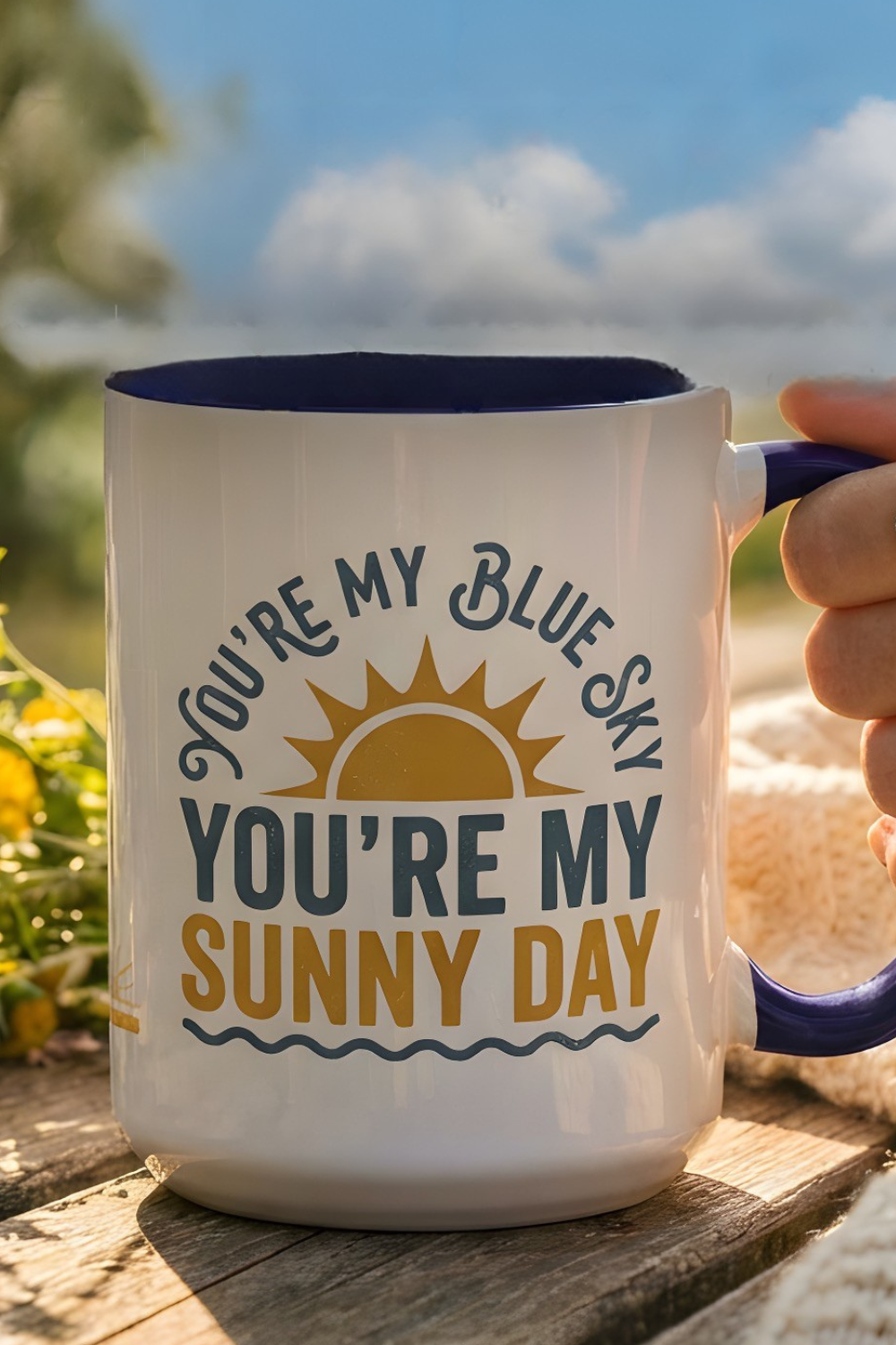 Mug with 'You're my blue sky, you're my sunny day' text and sun graphic on a wooden surface with a natural background.