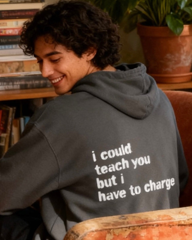 Person wearing a hoodie with text, sitting in a room with books and a plant.