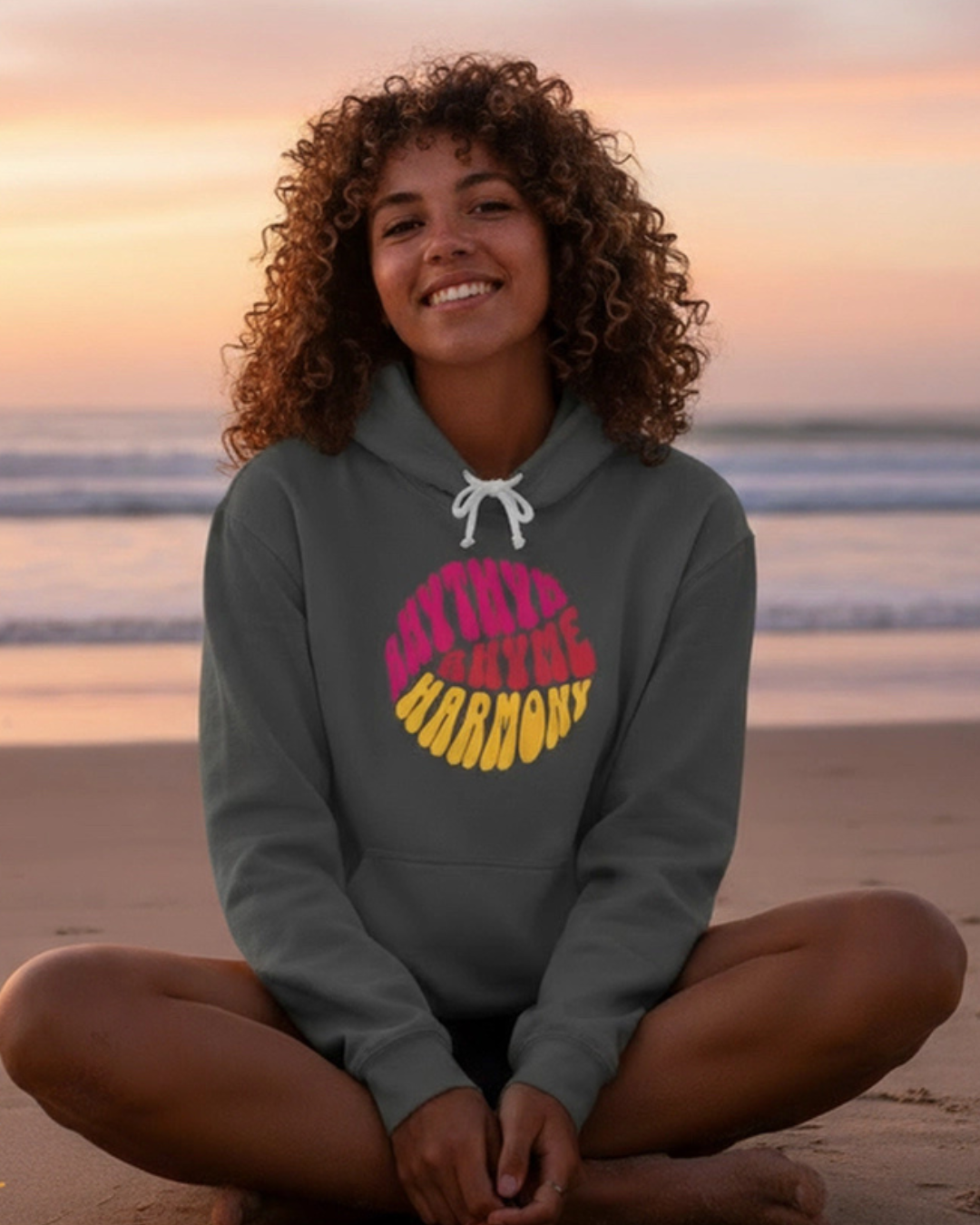 Person wearing a hoodie with colorful text on a beach at sunset