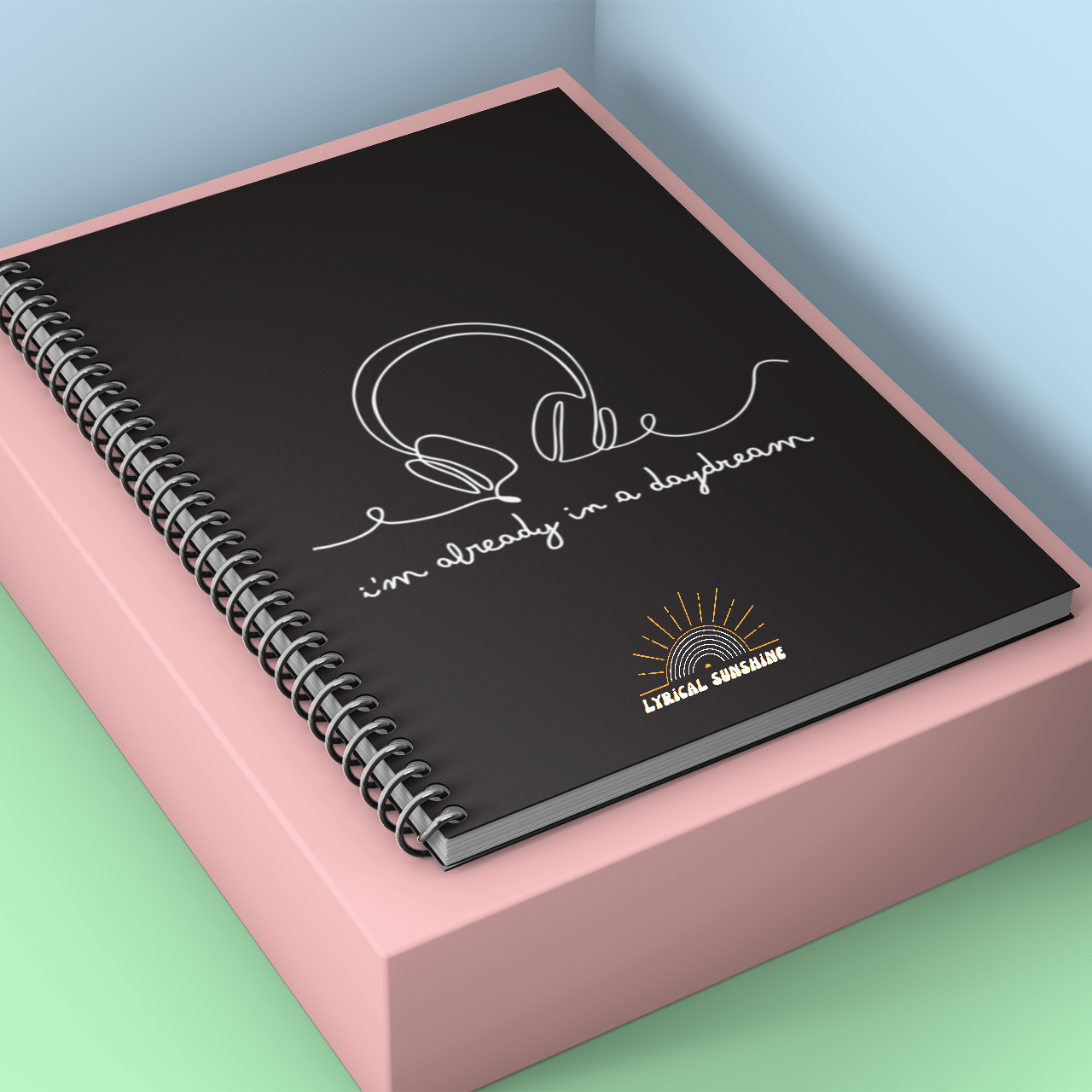 Black spiral-bound notebook with text on a pink stand against a light blue wall.