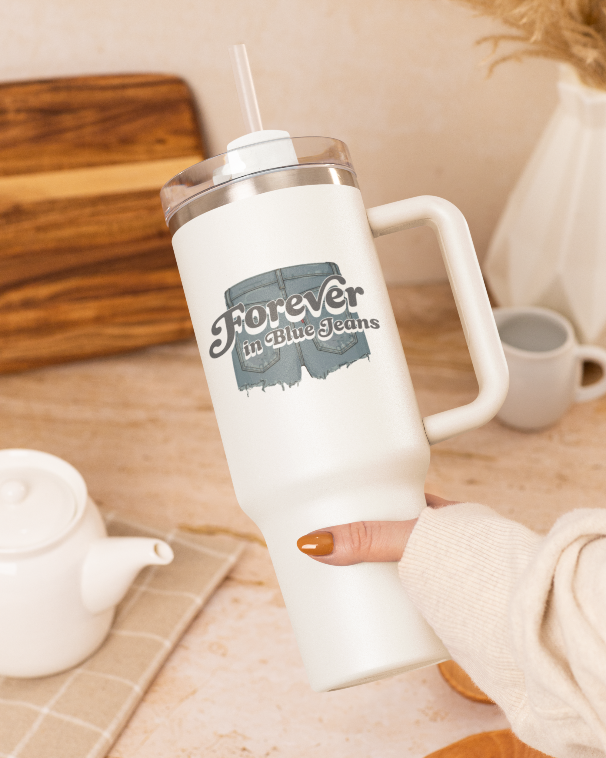 White tumbler with a handle and straw on a wooden table with a teapot and mug.