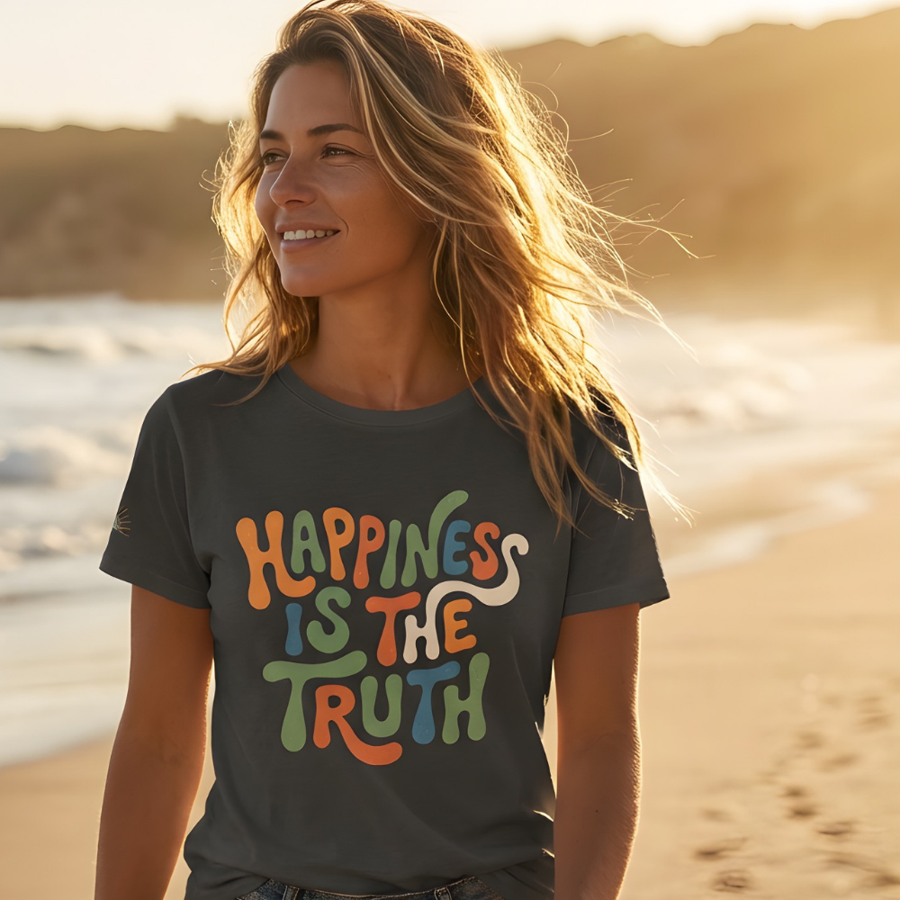 Woman on a beach wearing a t-shirt with 'Happiness is the truth' text, with a sunset in the background.