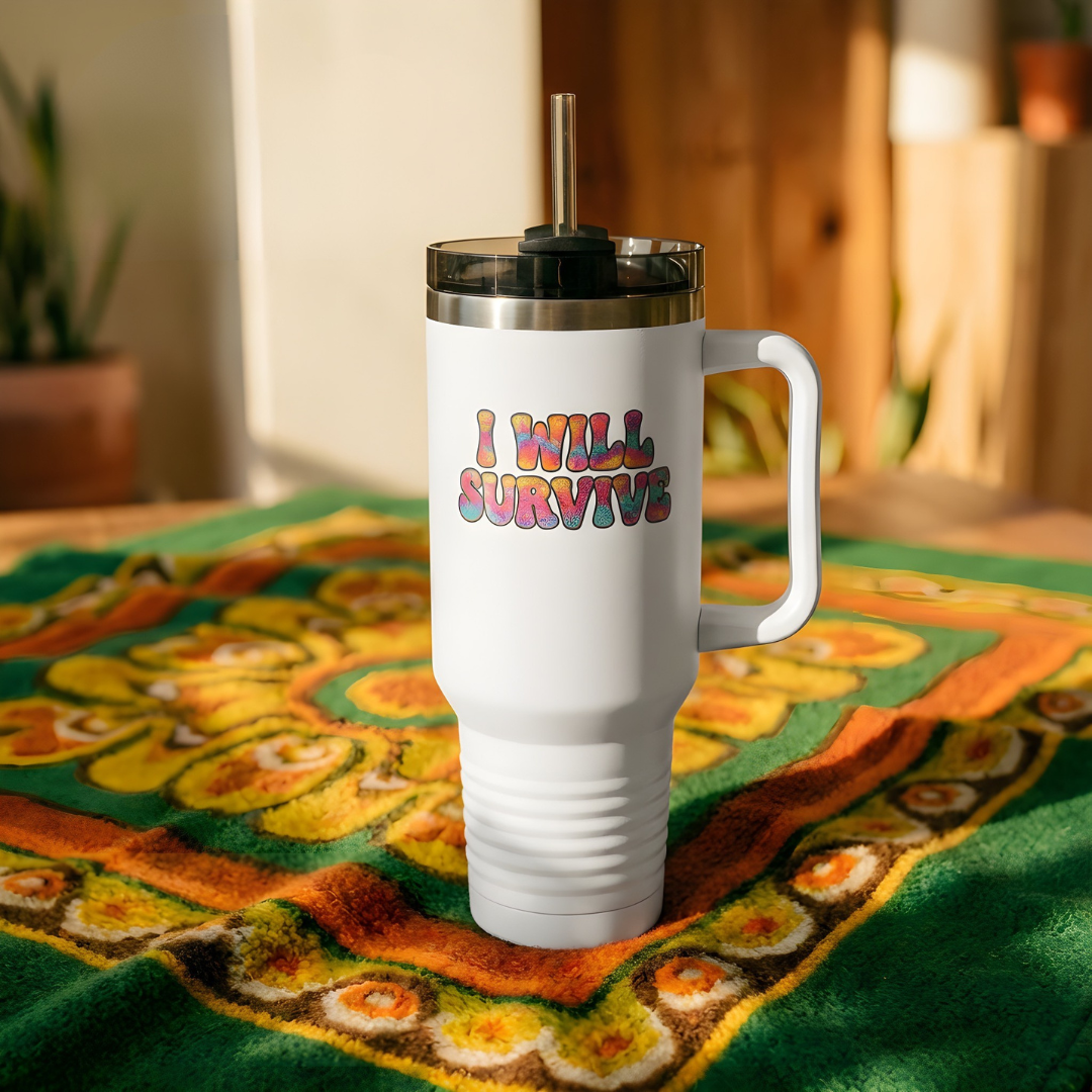 White travel mug with 'I Will Survive' text on a colorful fabric background