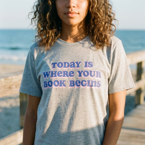 Person wearing a t-shirt with 'Today is where your book begins' text on a wooden pier by the ocean.