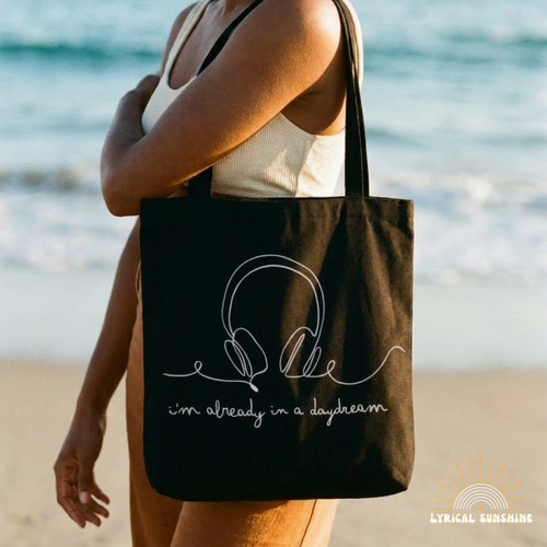 Woman holding a black tote bag with text on a beach