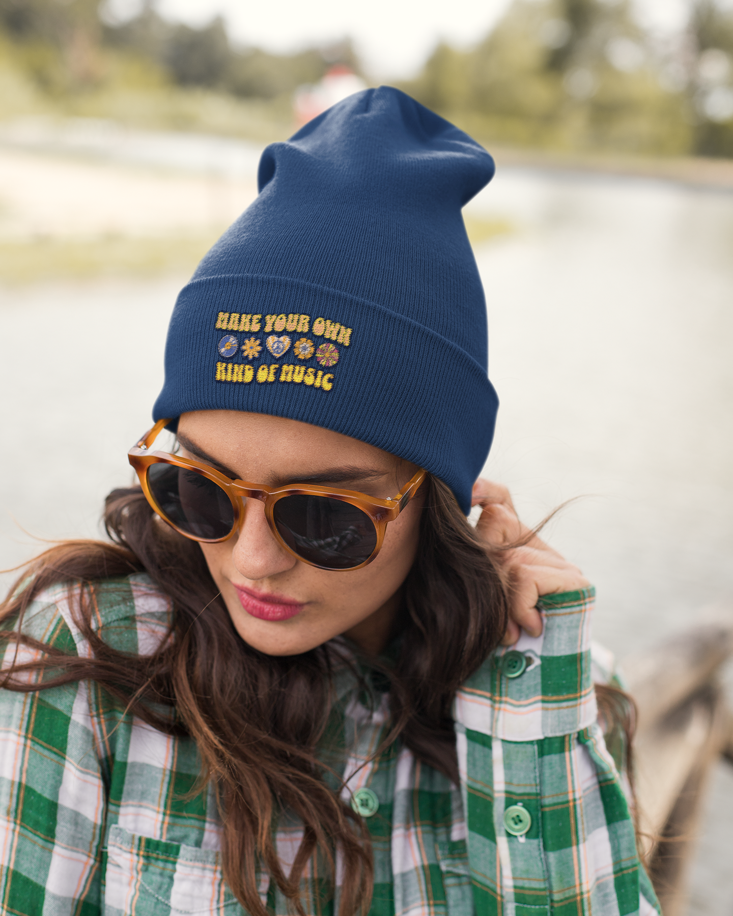 Woman wearing a blue beanie with text and sunglasses, standing by a body of water.