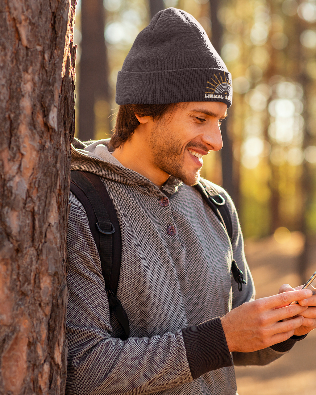 Man leaning against a tree in a forest, using a smartphone