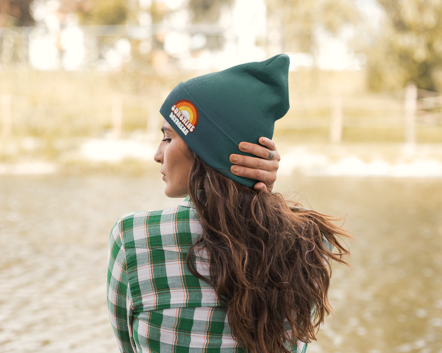 Person wearing a green beanie and plaid shirt by a body of water
