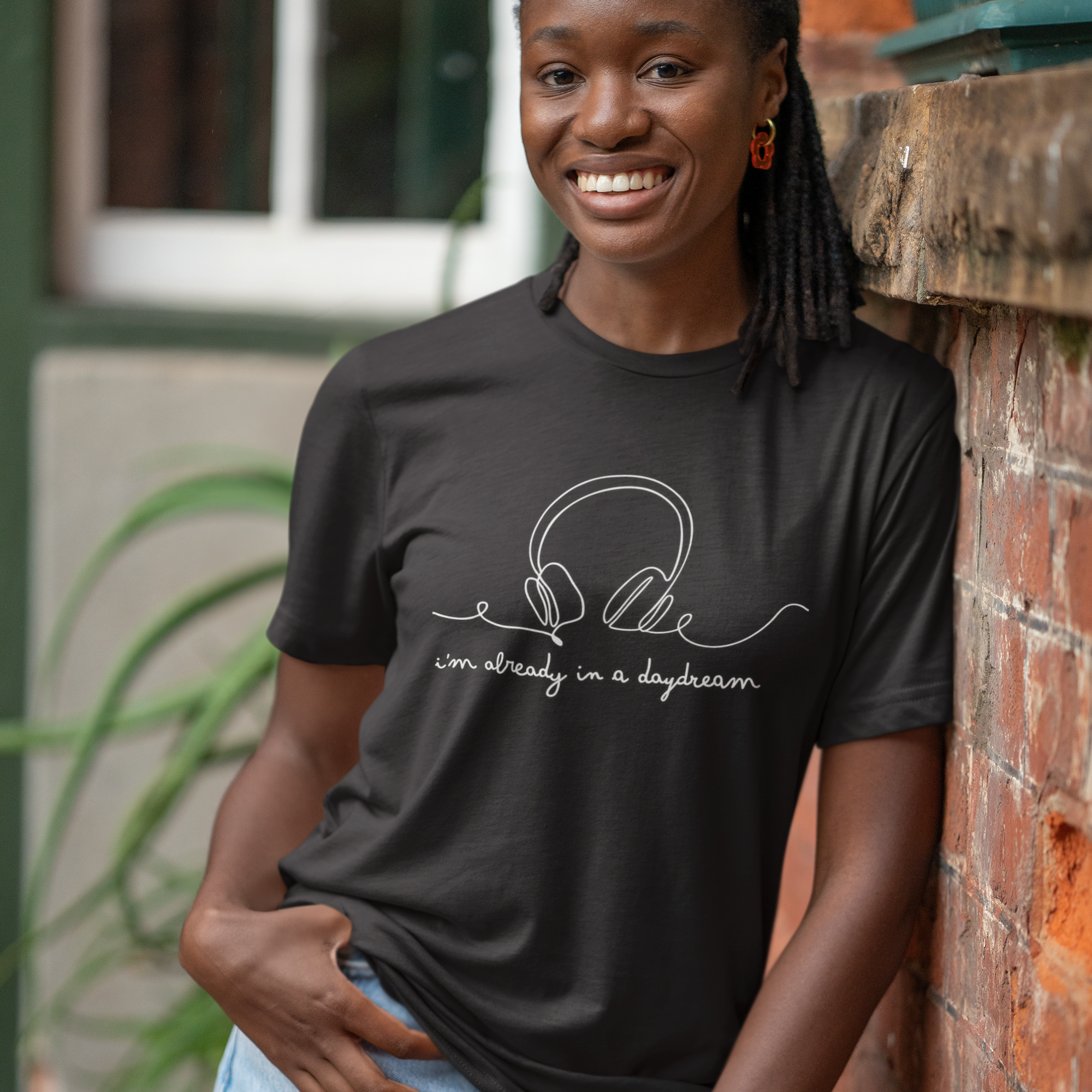 Woman wearing a black t-shirt with text, standing against a brick wall.