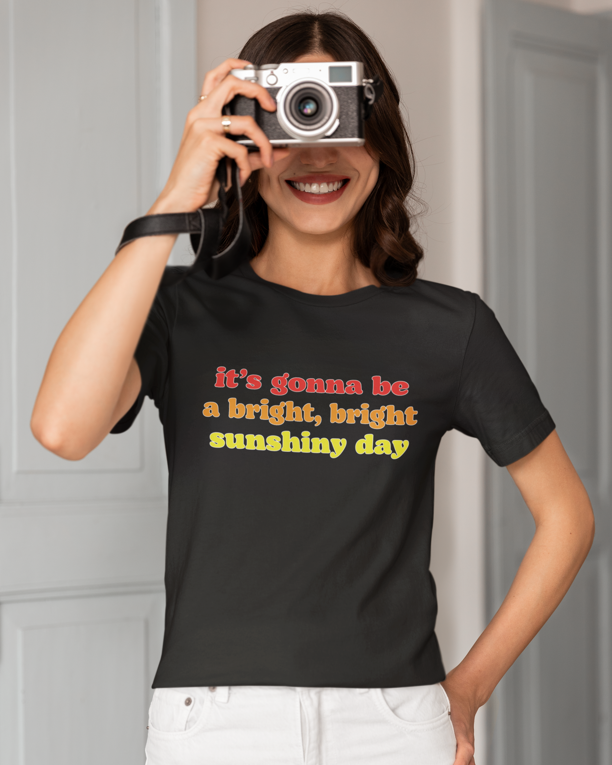Person wearing a black t-shirt with a motivational quote, holding a camera.