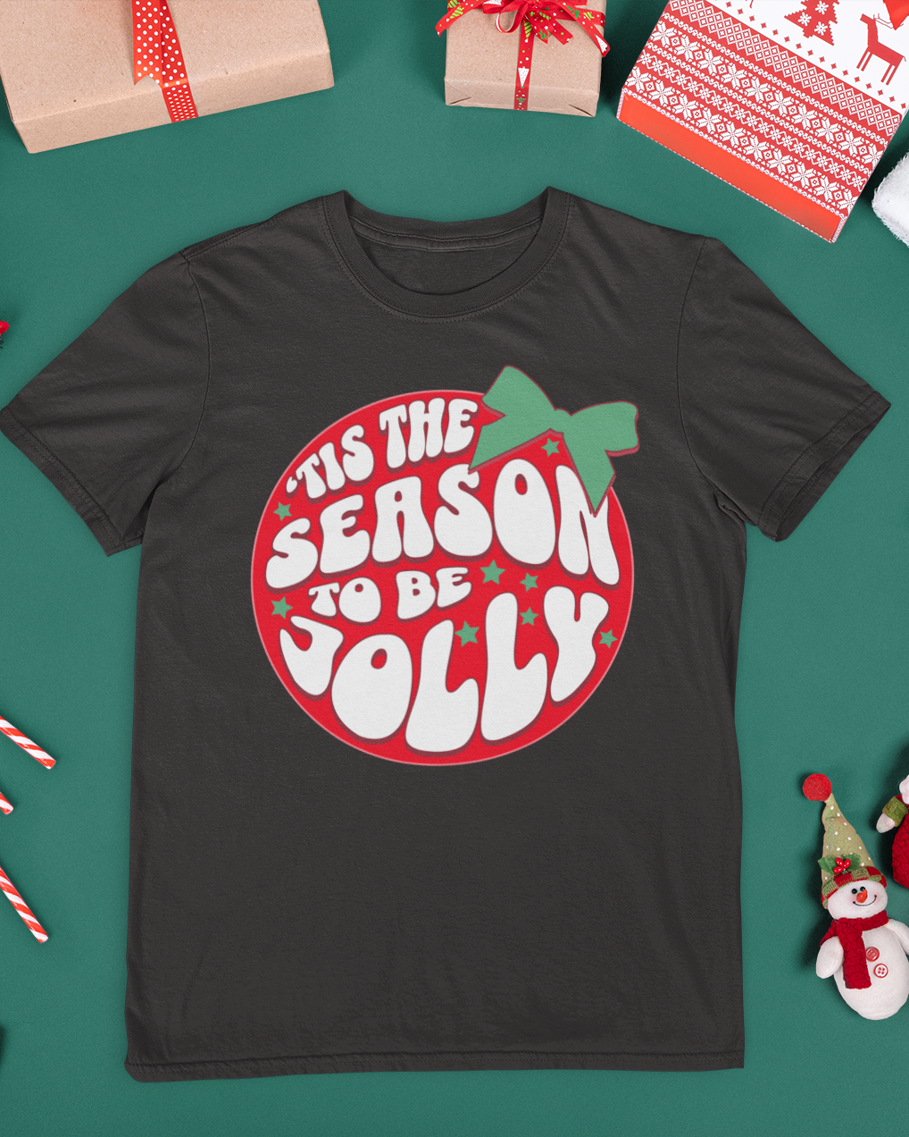 Black t-shirt with Christmas design surrounded by festive items on a green background