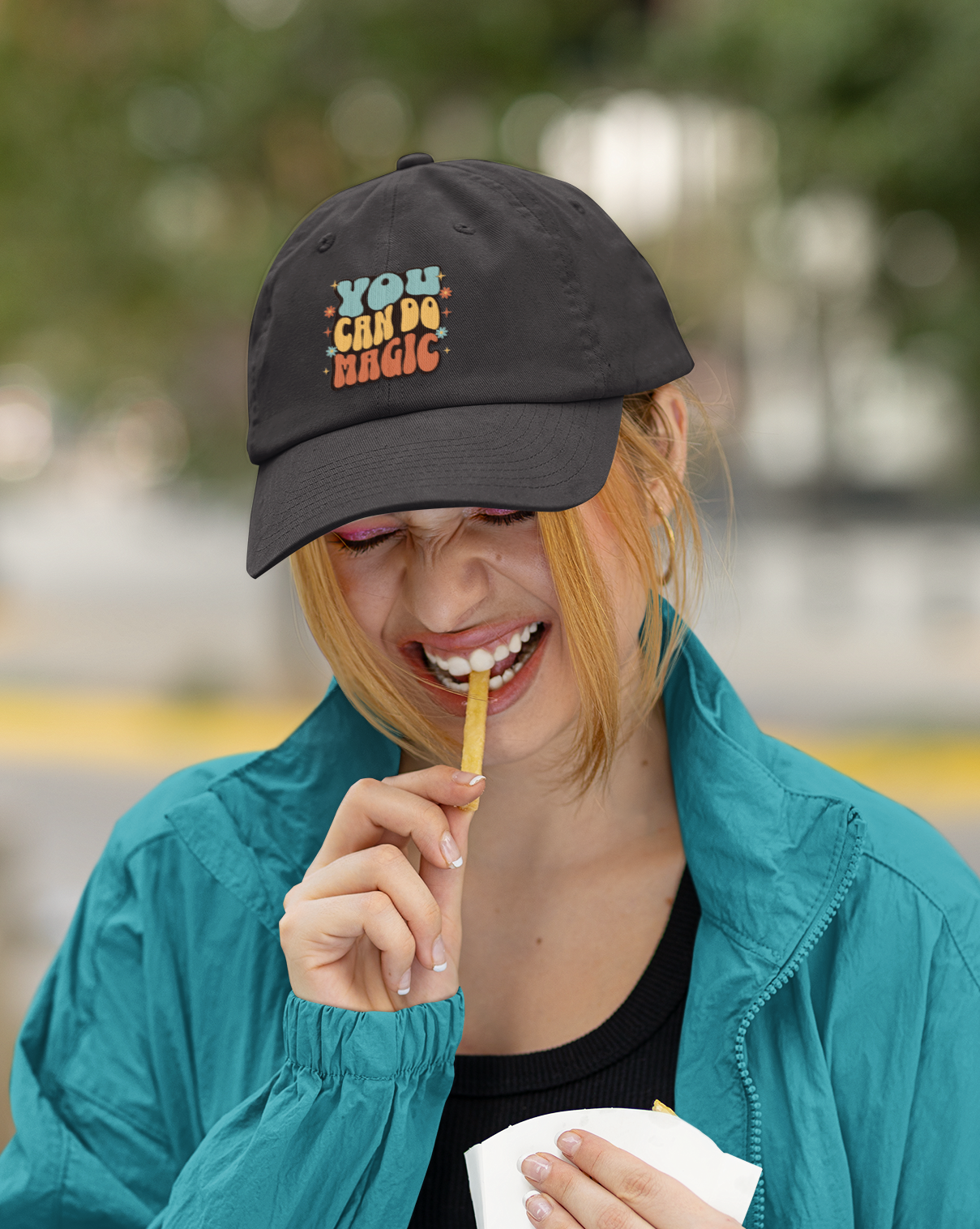 Woman wearing a black cap with text, eating a snack outdoors.