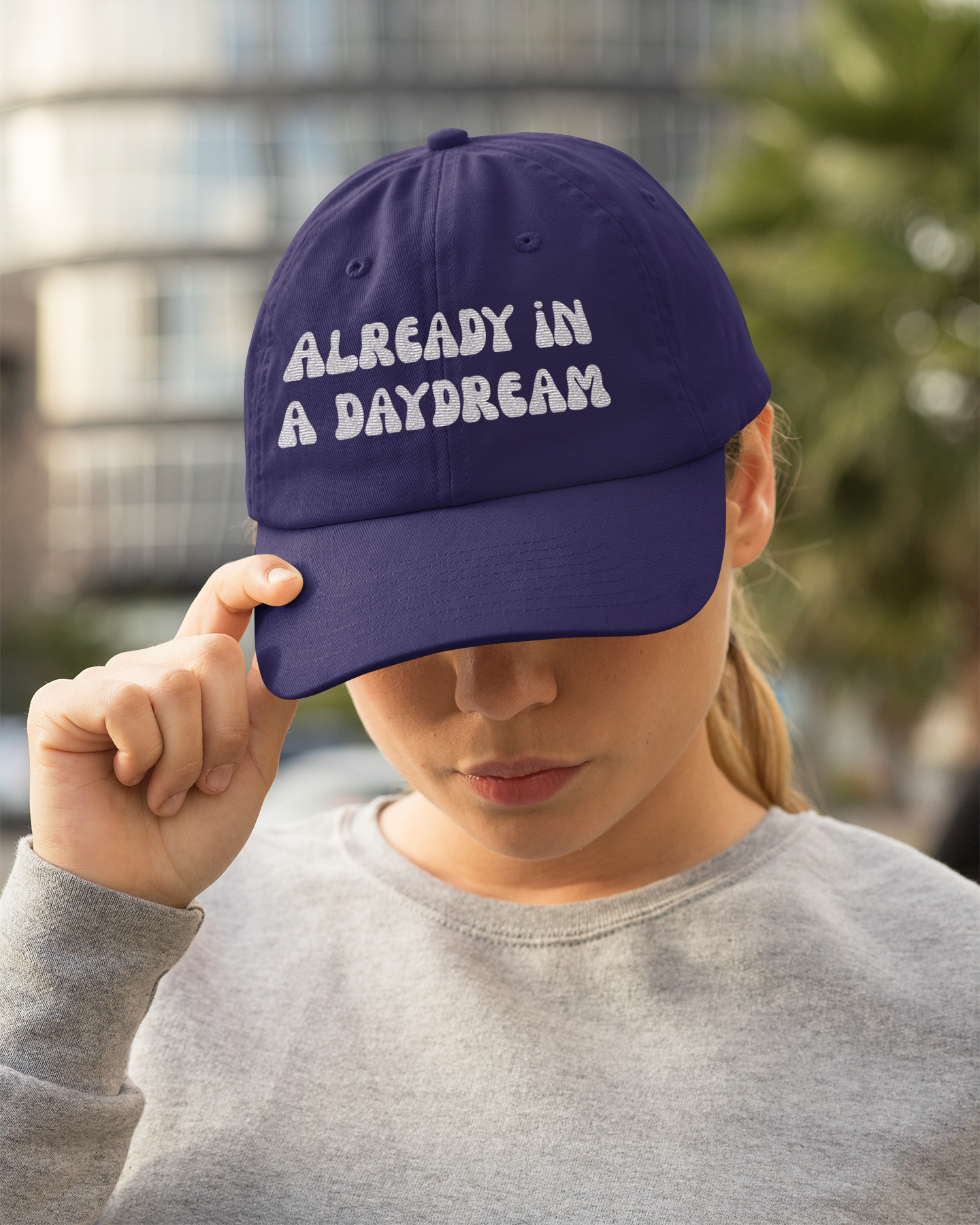 Person wearing a purple cap with 'ALREADY IN A DAYDREAM' text, blurred background