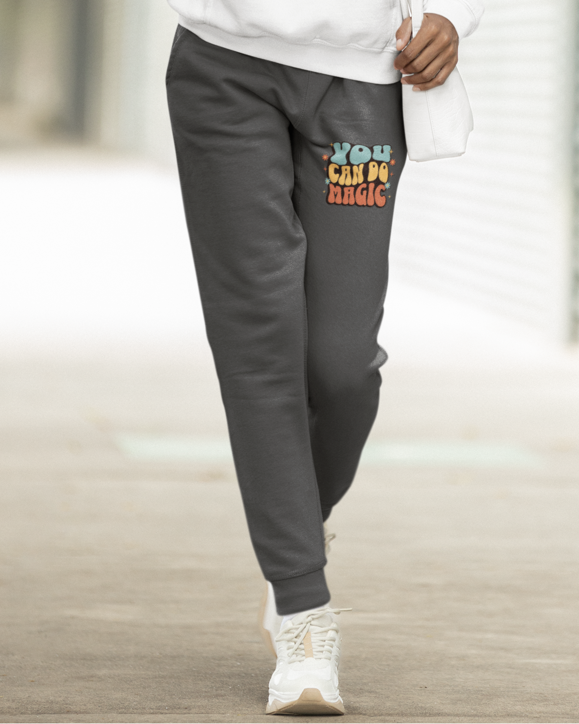 Person wearing a white hoodie and gray sweatpants with colorful text, holding a cup.