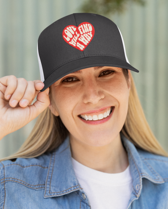 Person wearing a black cap with a red heart design, smiling outdoors.