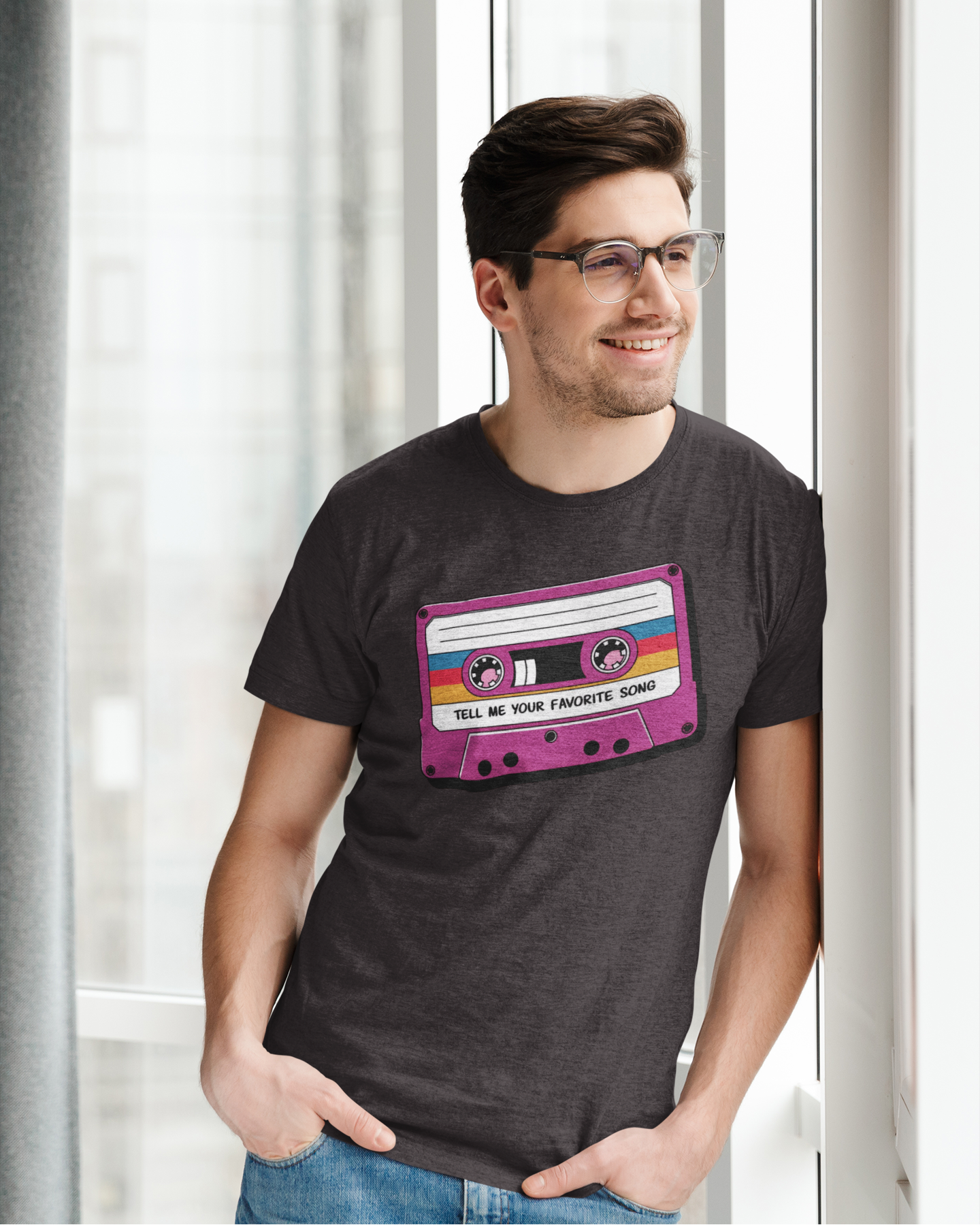 Man wearing a t-shirt with a cassette tape design in front of a window.