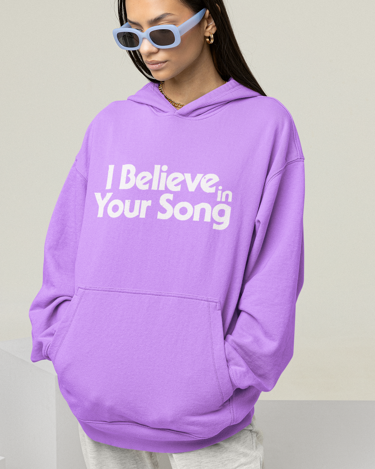 Person wearing a purple hoodie with 'I Believe in Your Song' text on a plain background