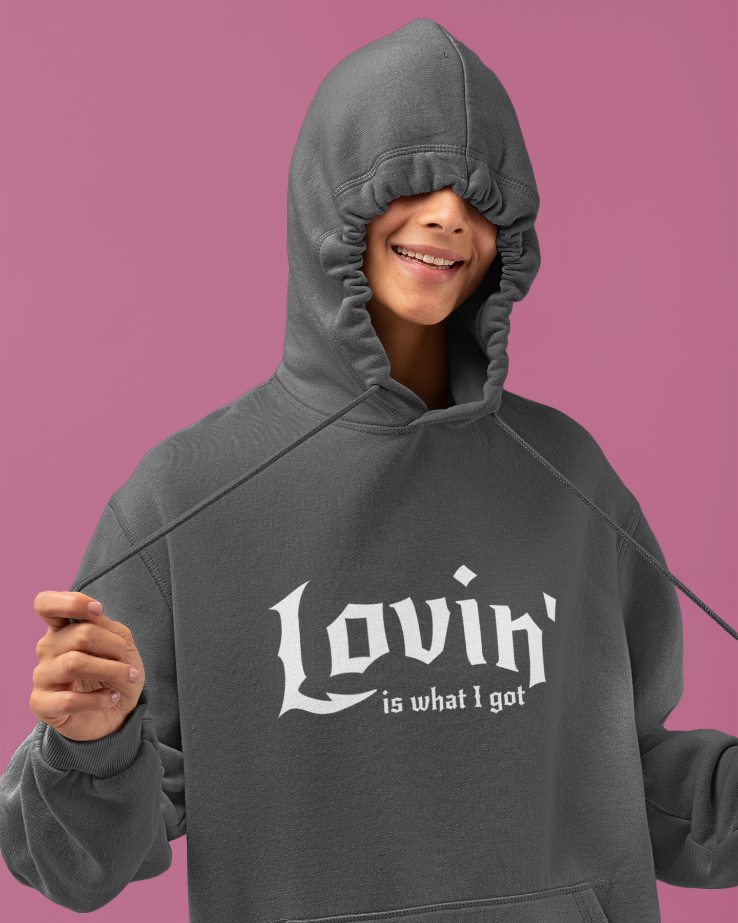 Person wearing a gray hoodie with 'Lovin' is what I got' text on a pink background