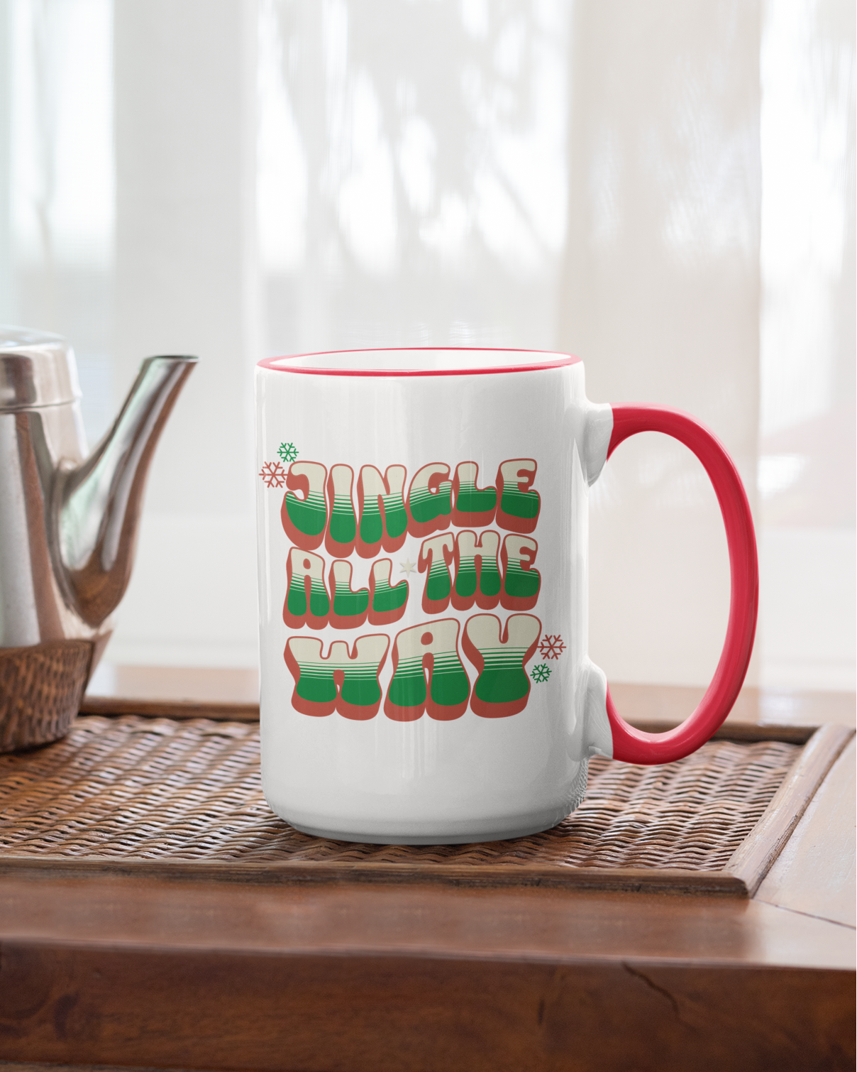 White mug with red handle and colorful text on a wooden table with a teapot.