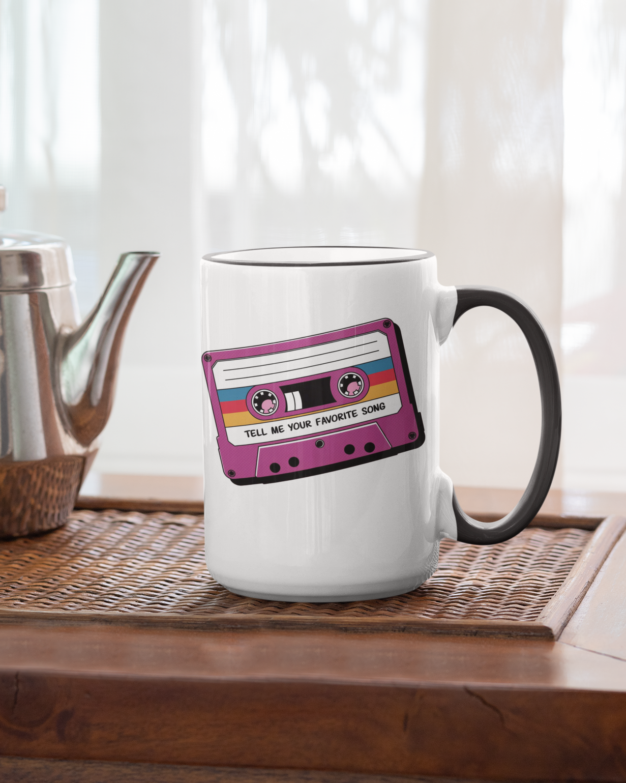 White mug with a cassette tape design on a wooden table with a teapot.