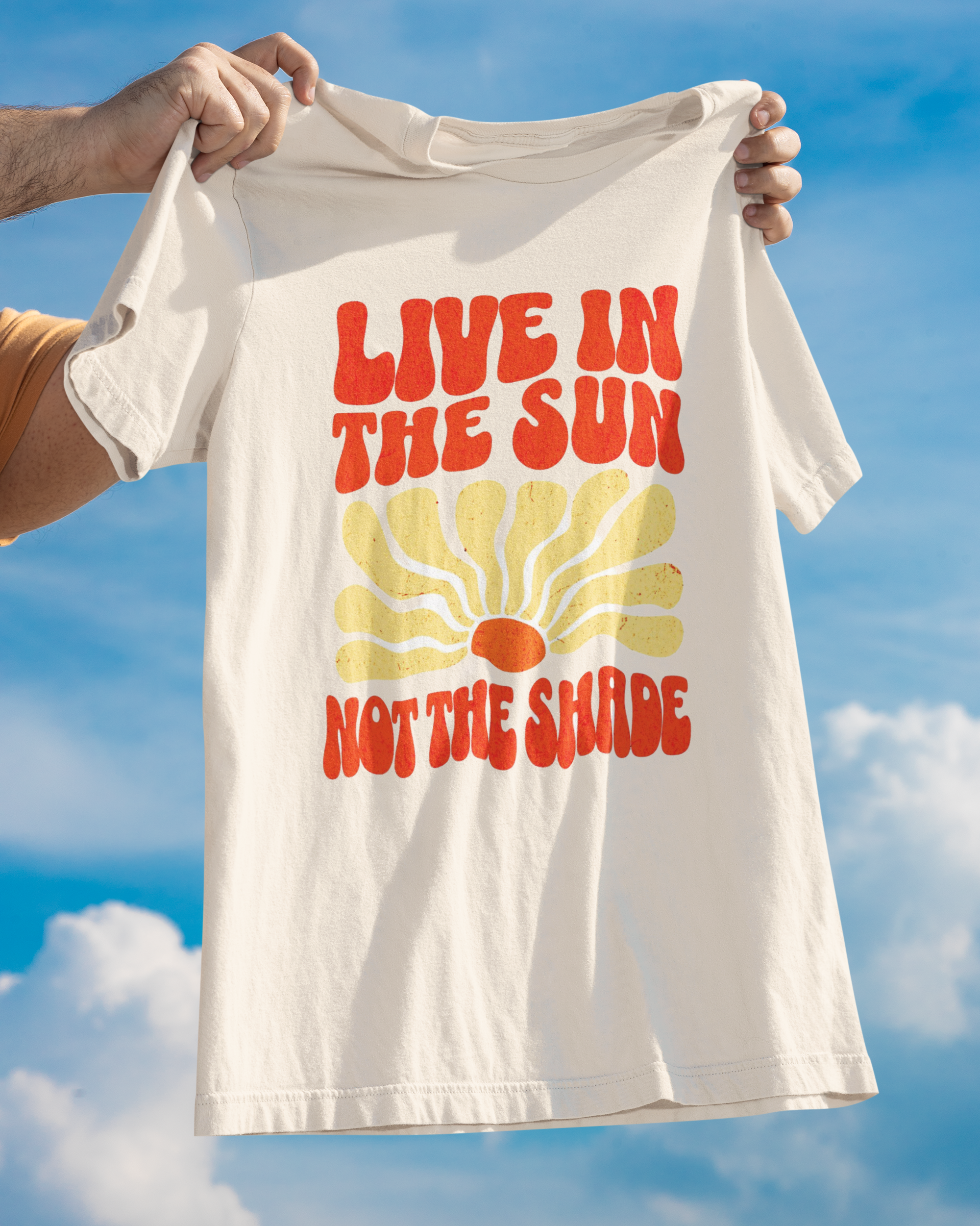 T-shirt with 'Live in the sun, not the shade' text held against a blue sky.