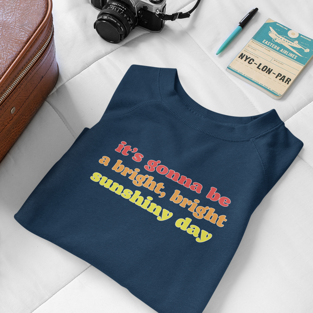 Folded navy blue t-shirt with text on a white surface with travel items around