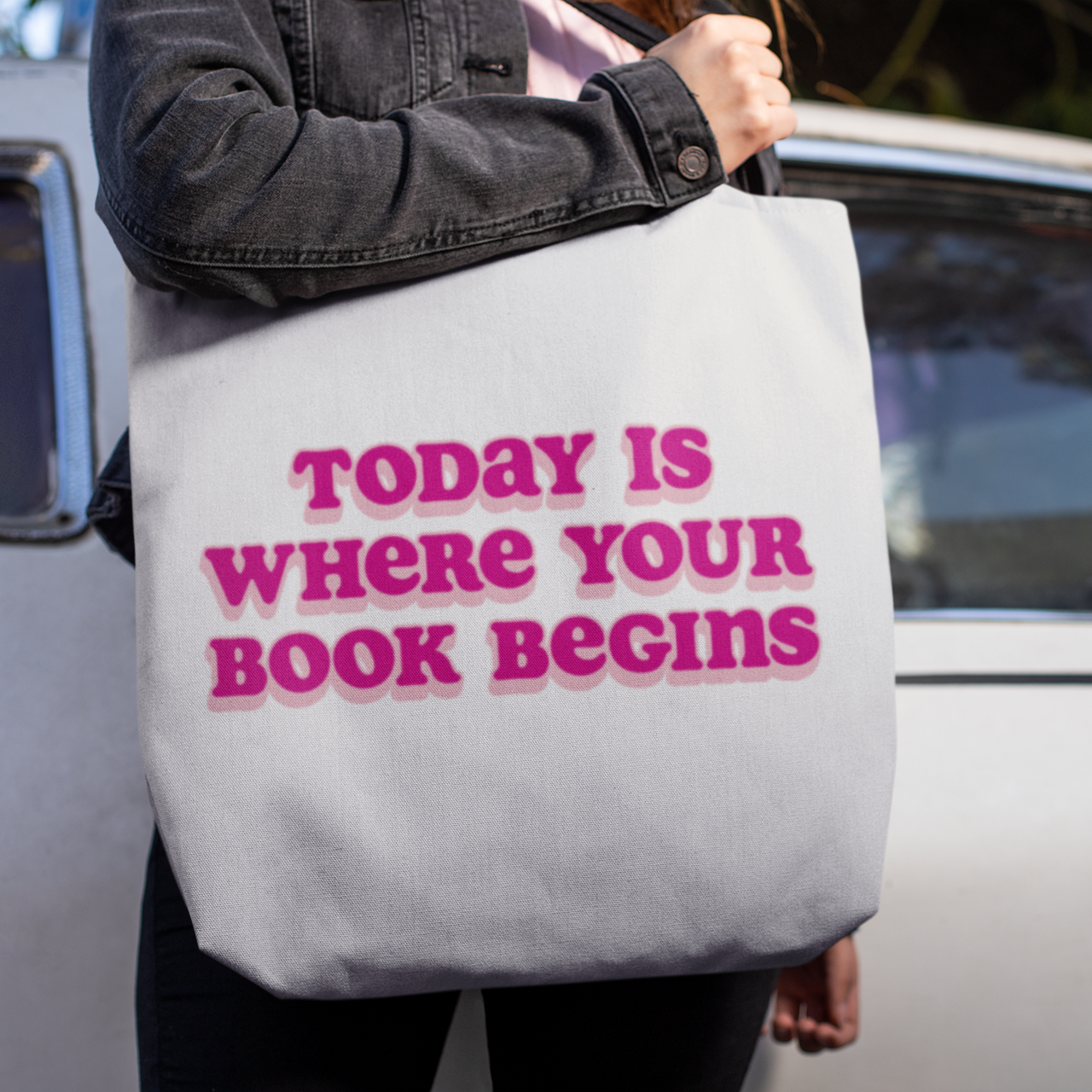 Person holding a tote bag with 'Today is where your book begins' text.