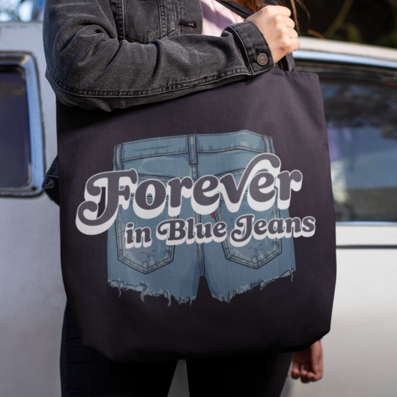 Person holding a tote bag with 'Forever in Blue Jeans' text and graphic.