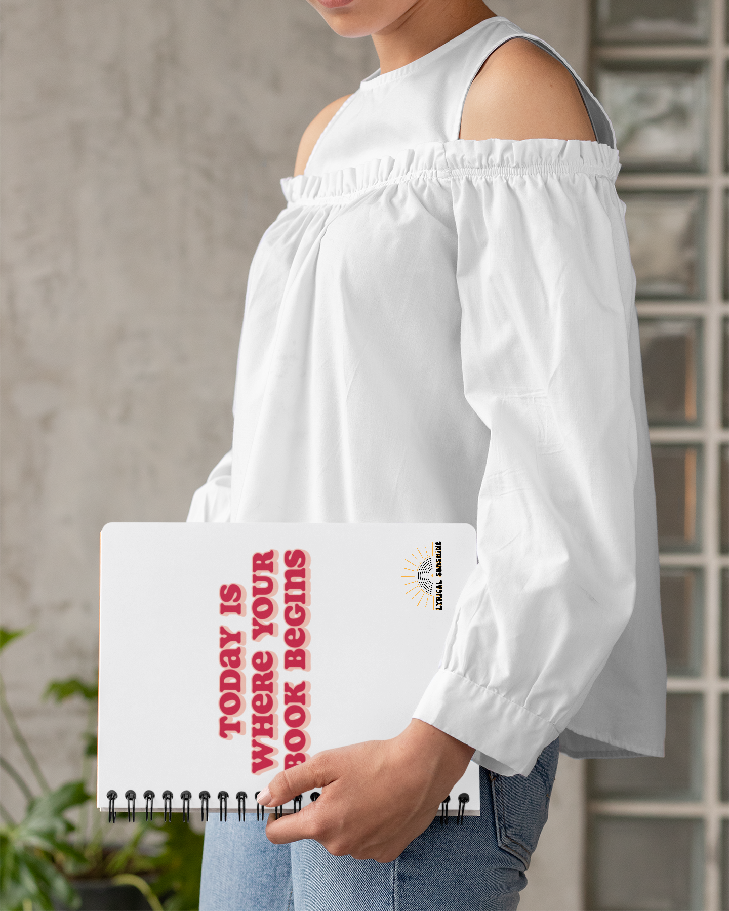 Person holding a notebook with motivational text, wearing a white off-shoulder top.