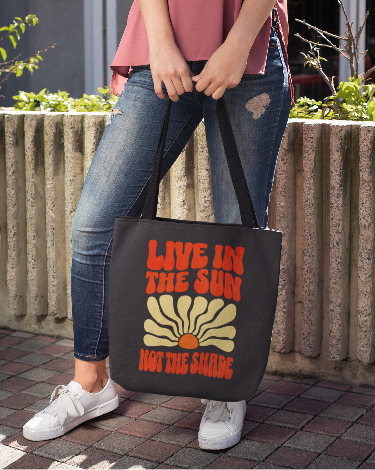 Person holding a black tote bag with a sun design and text outdoors.