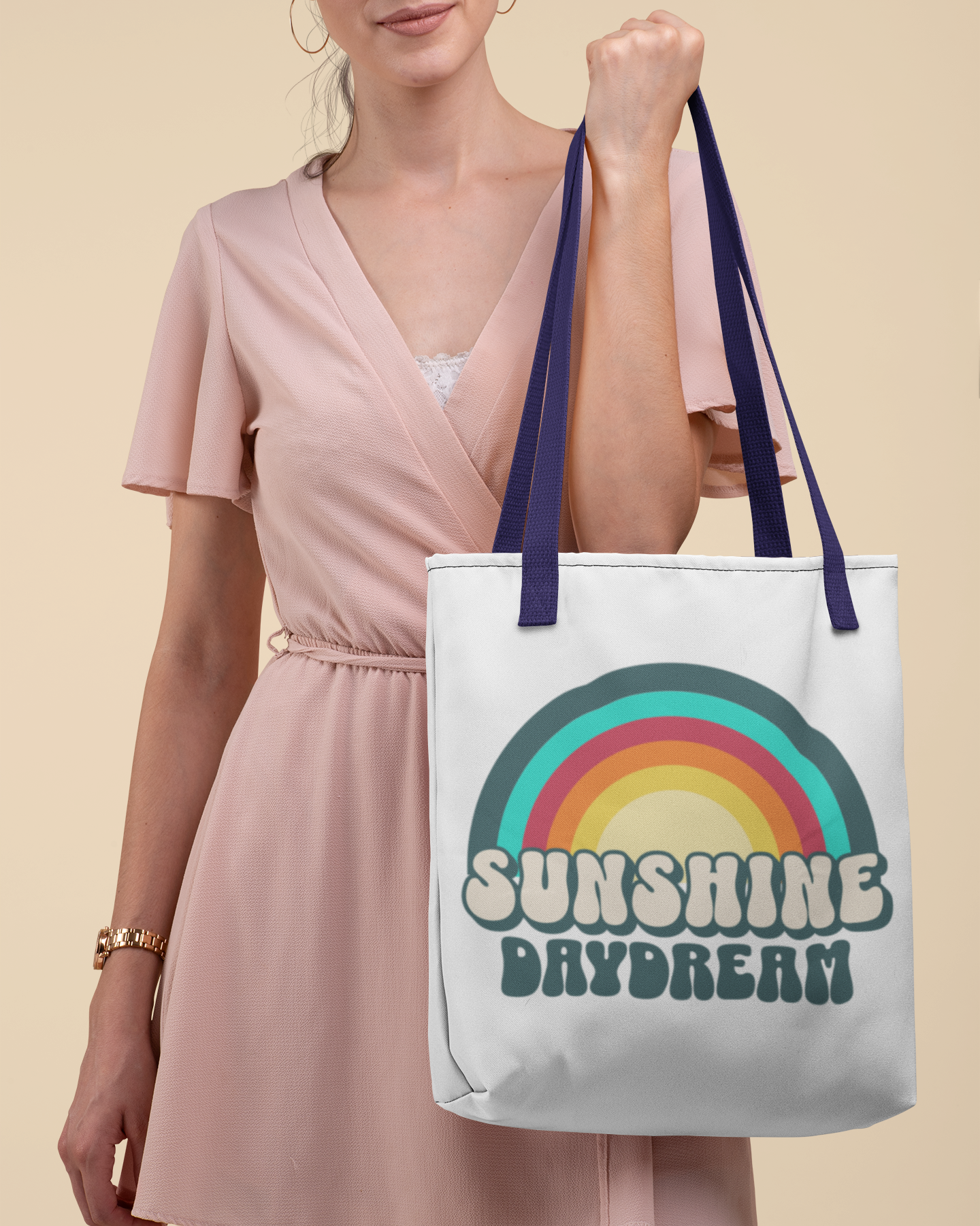 Woman holding a tote bag with a rainbow design and 'Sunshine Daydream' text on a beige background