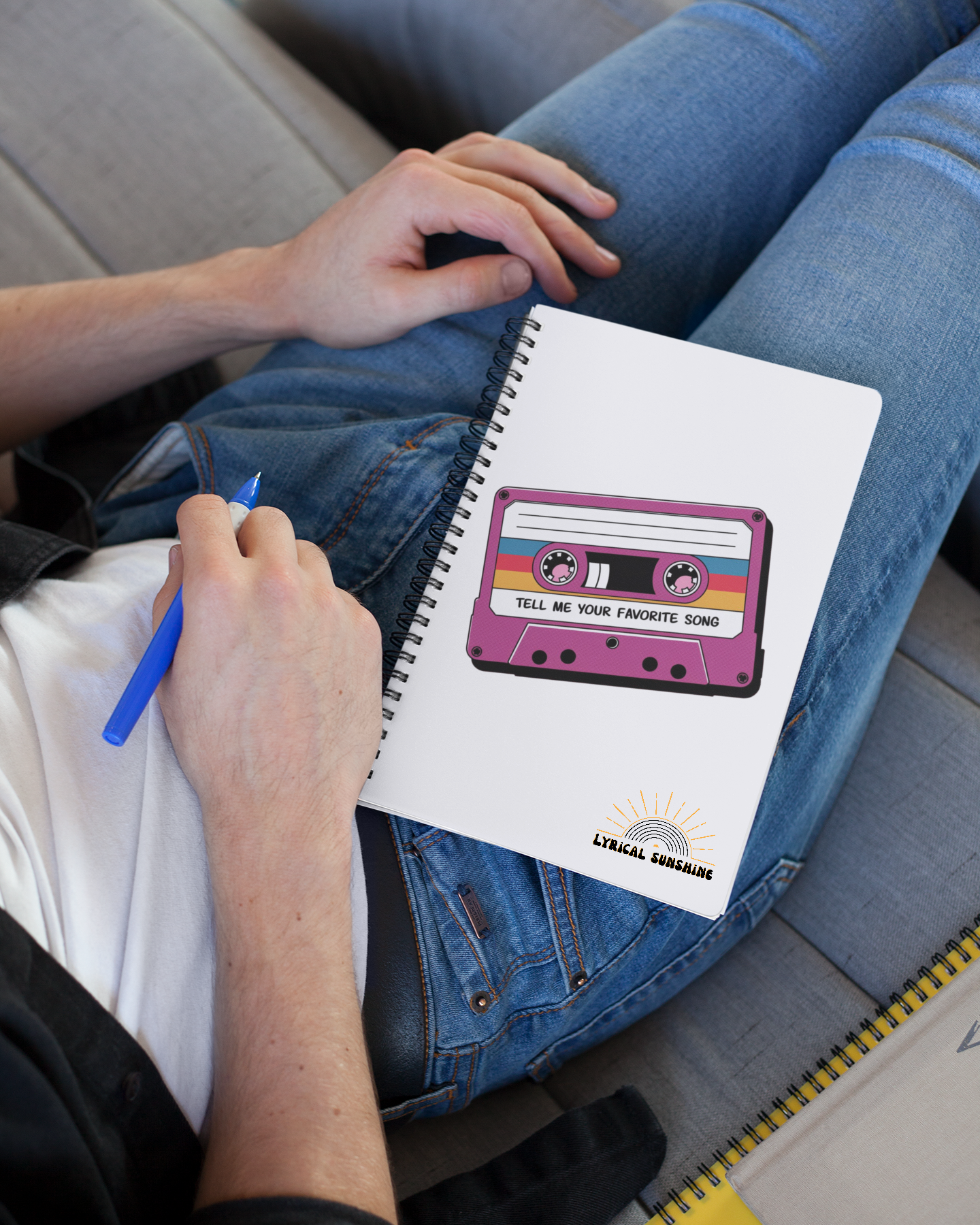 Person sitting on a couch with a notebook featuring a cassette tape design.