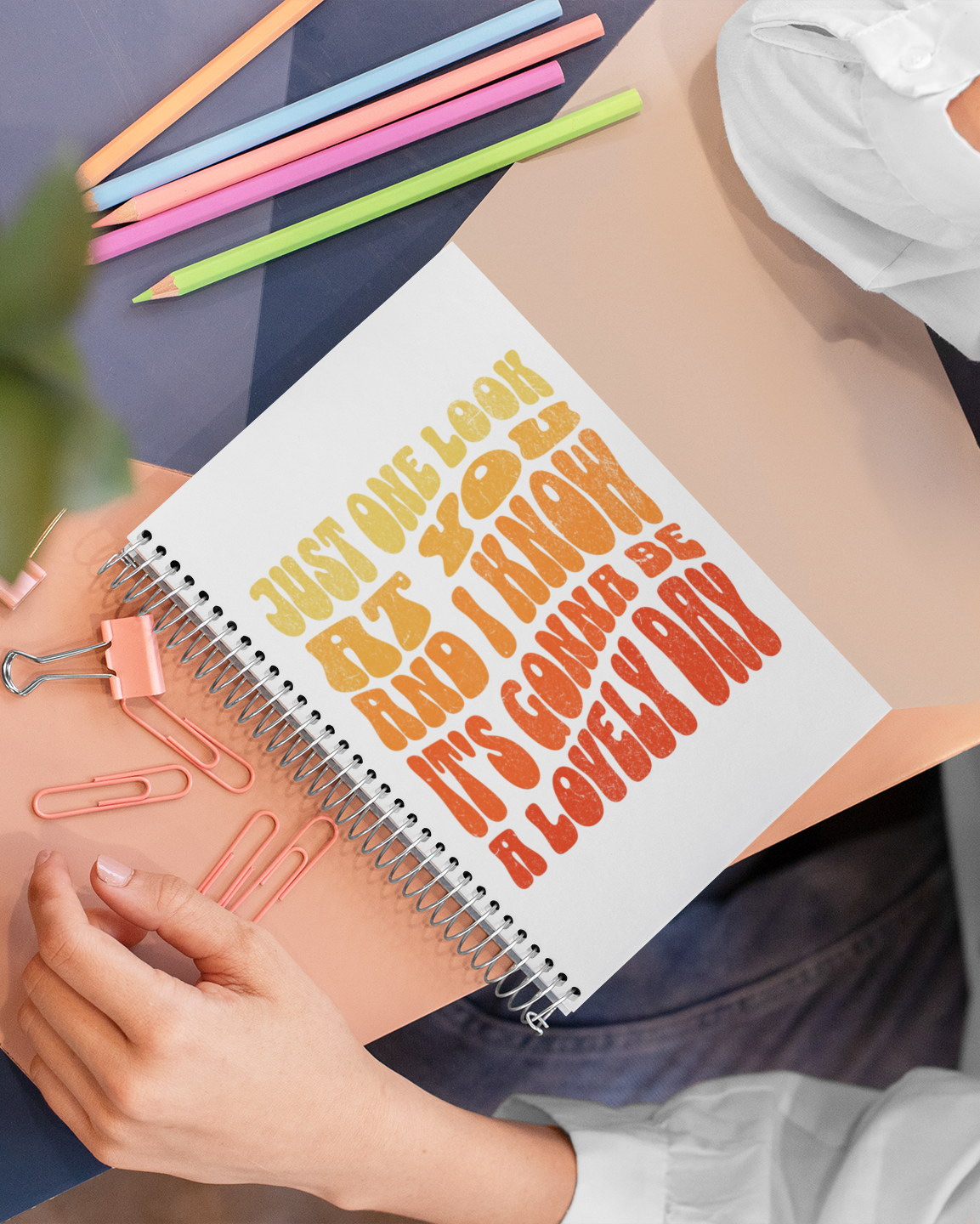Person holding a notebook with colorful text and stationery items.