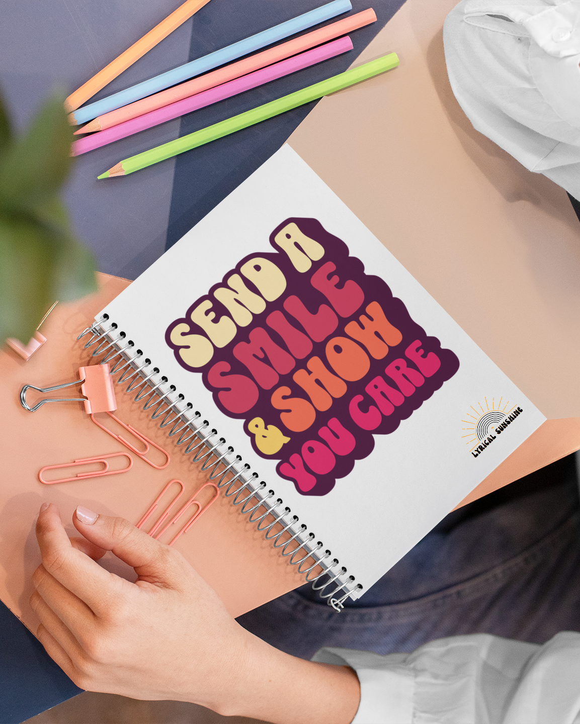 Notebook with motivational quote held by a person, surrounded by stationery items.