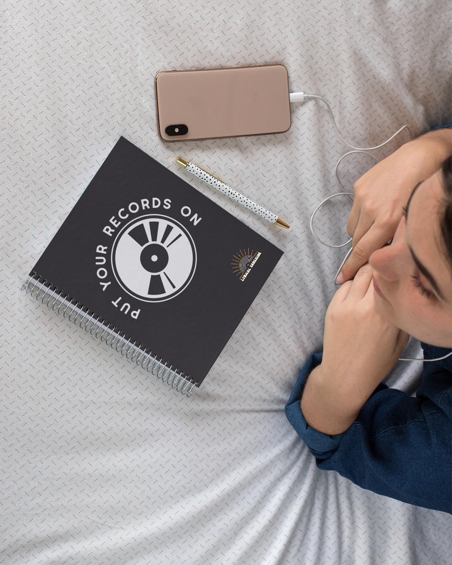 Person lying on a bed with a notebook, pen, and phone next to them.