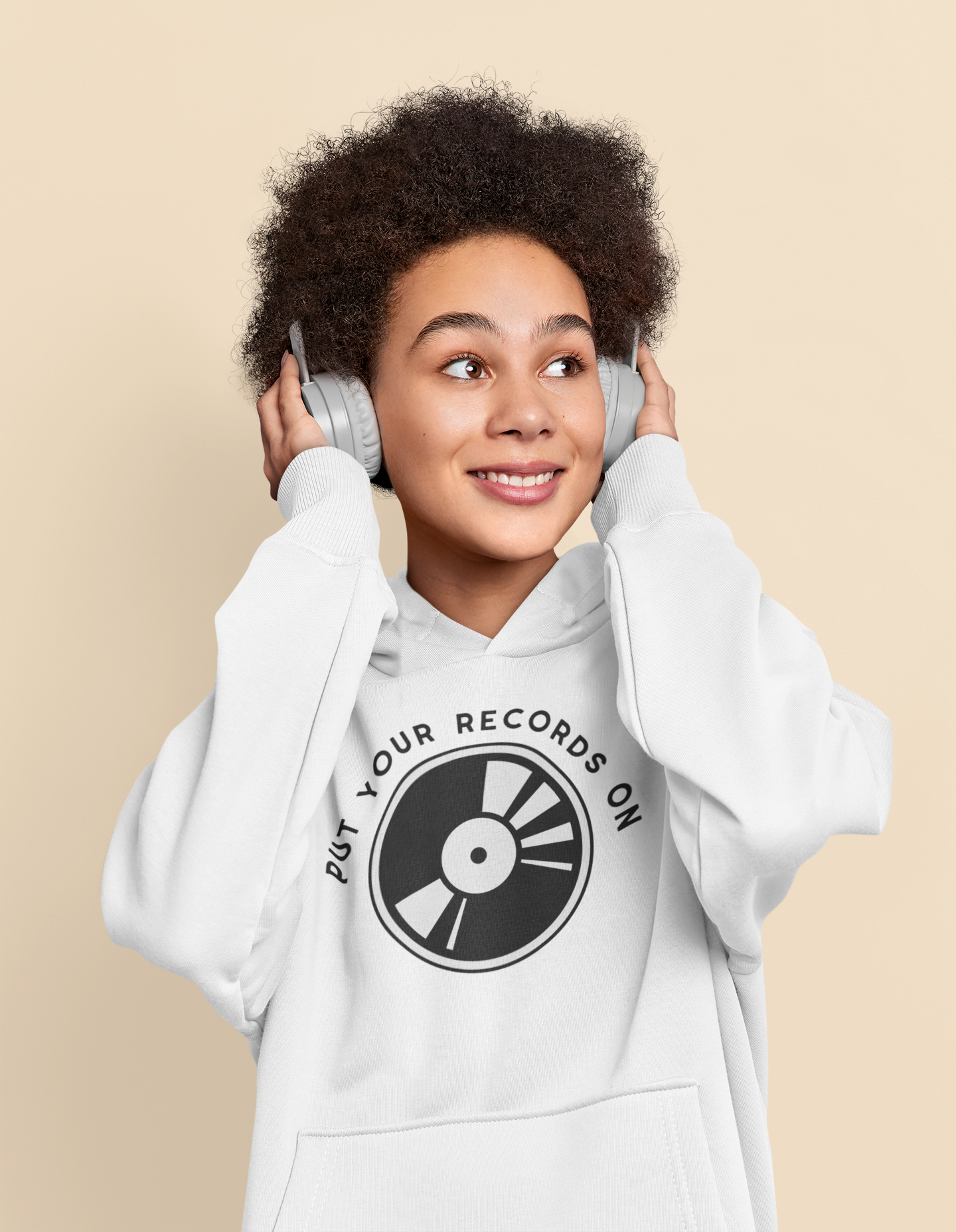 Person wearing a white hoodie with a vinyl record design and text, listening to music with headphones on a beige background.