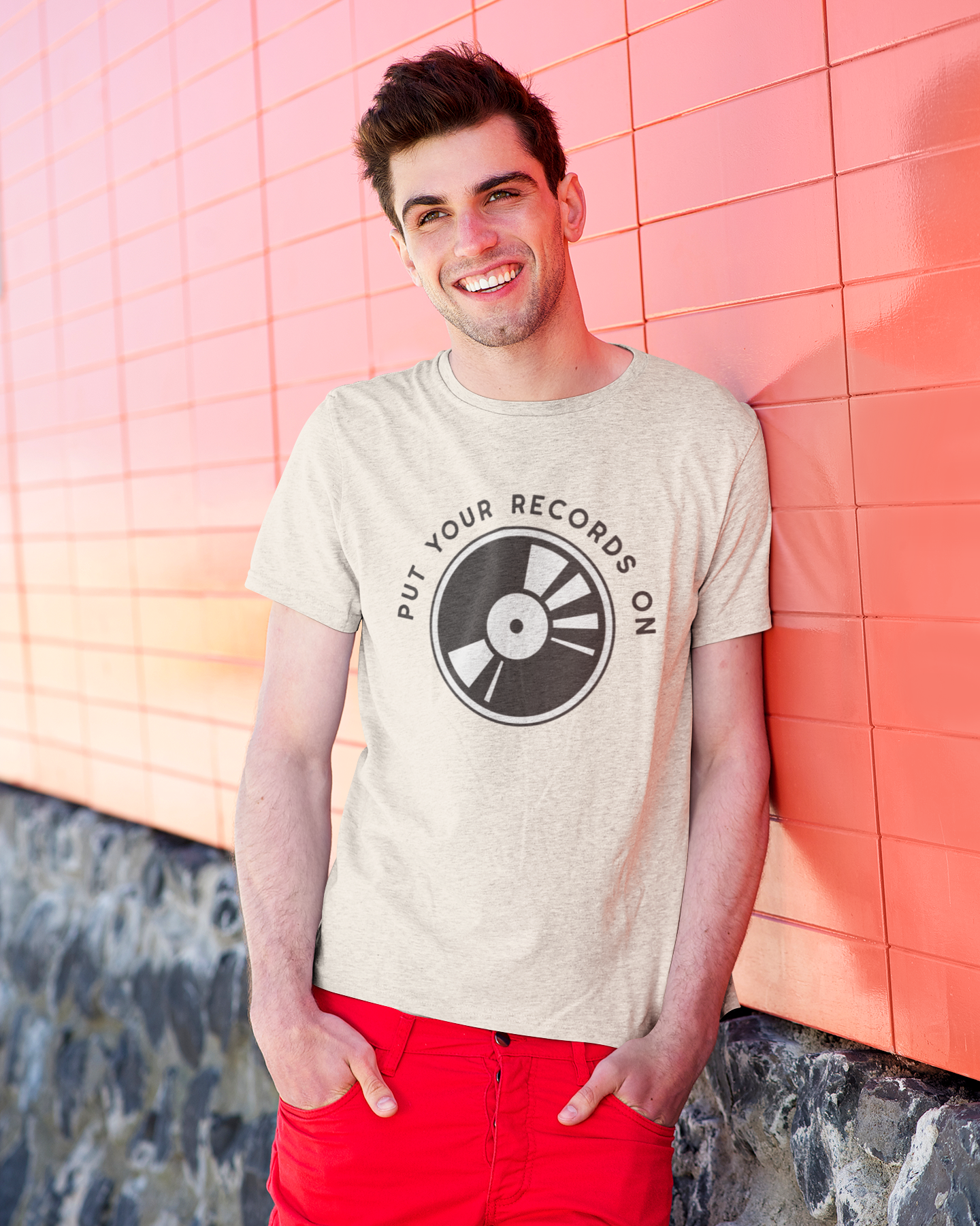 Man wearing a t-shirt with a vinyl record design against a pink tiled wall.